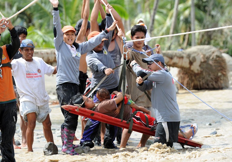 Lenlen Medrano and her child, survivors of Typhoon Bopha, are transported on a stretcher across a surging river by zip line in the town of New Bataan...