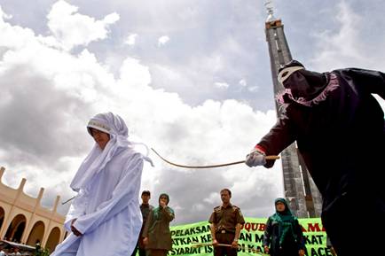 A masked and hooded person canes Indonesian food seller Murni Amris for violating Shariah law outside a mosque in Jantho, Aceh, in this October 1, 2010 file photo. (AFP Photo/Chaideer Mahyuddin) 